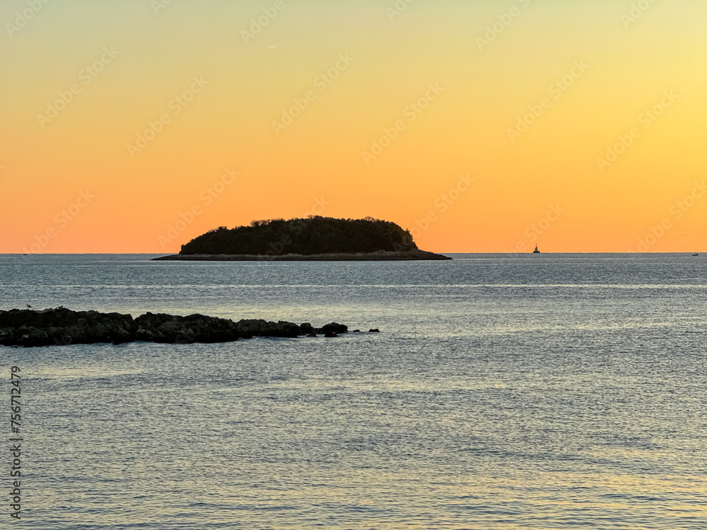 Watching dramatic sunset at coastal village Funtana, Istria, Croatia, EU. Silhouette of remote tropical island. Calm sea surface reflects vibrant colors of sky. Vacation at Adriatic Mediterranean Sea