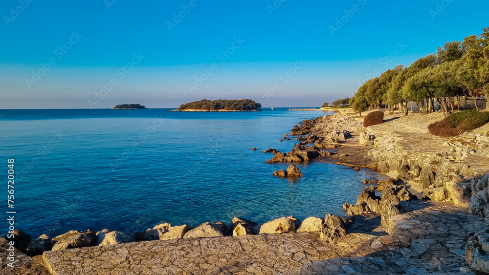 Panoramic view of small islands seen from pebble beach in coastal town Funtana, Istria, Croatia. Calm sea surface of Adriatic Mediterranean Sea in morning hours. Seaside vacation concept in summer