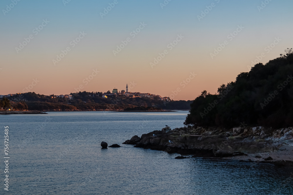 Distant view of church in Vrsar during dramatic sunset in coastal village Funtana, Istria, Croatia, EU. Calm sea surface reflects vibrant colors of sky. Vacation Adriatic Mediterranean Sea in summer