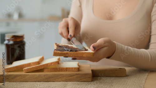 Cropped view female hands spread chocolate paste on slice toast with knife put peanut butter on bread close up. Unrecognizable woman in kitchen cooking breakfast sweet sandwich buy food with delivery