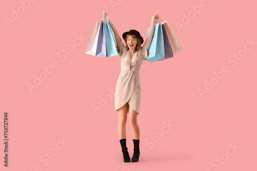 Beautiful happy young woman with shopping bags on pink background