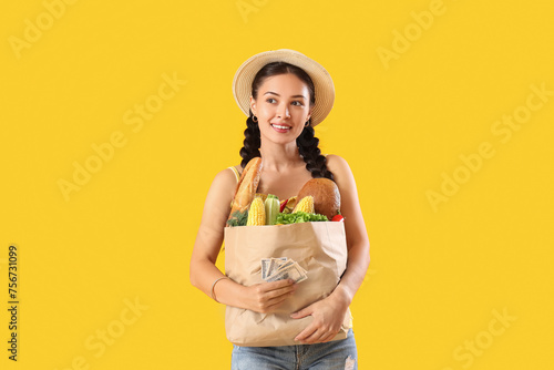 Beautiful young Asian woman with bag full of fresh products on yellow background