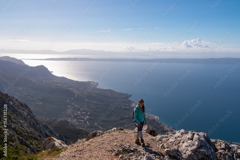 Hiker woman on top of mount Sinjal overlooking Biokovo nature park, Makarska, Dalmatia, Croatia. Scenic hiking trail in karst landscape. Dinaric Alps in summer. Coastline Adriatic Mediterranean Sea