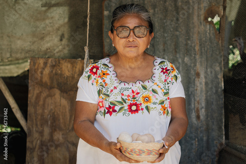 Portrait of a Latina woman looking at the camera and holding a basket of eggs collected from a chicken coop.