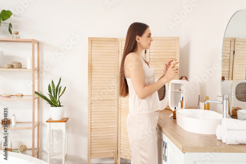 Beautiful young woman with jar of cream and small refrigerator for cosmetic products in bathroom