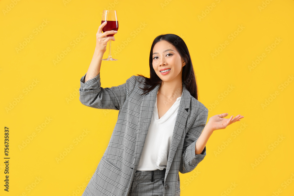 Beautiful Asian businesswoman with glass of red wine on yellow background Beautiful Asian businesswoman with glass of red wine on yellow background