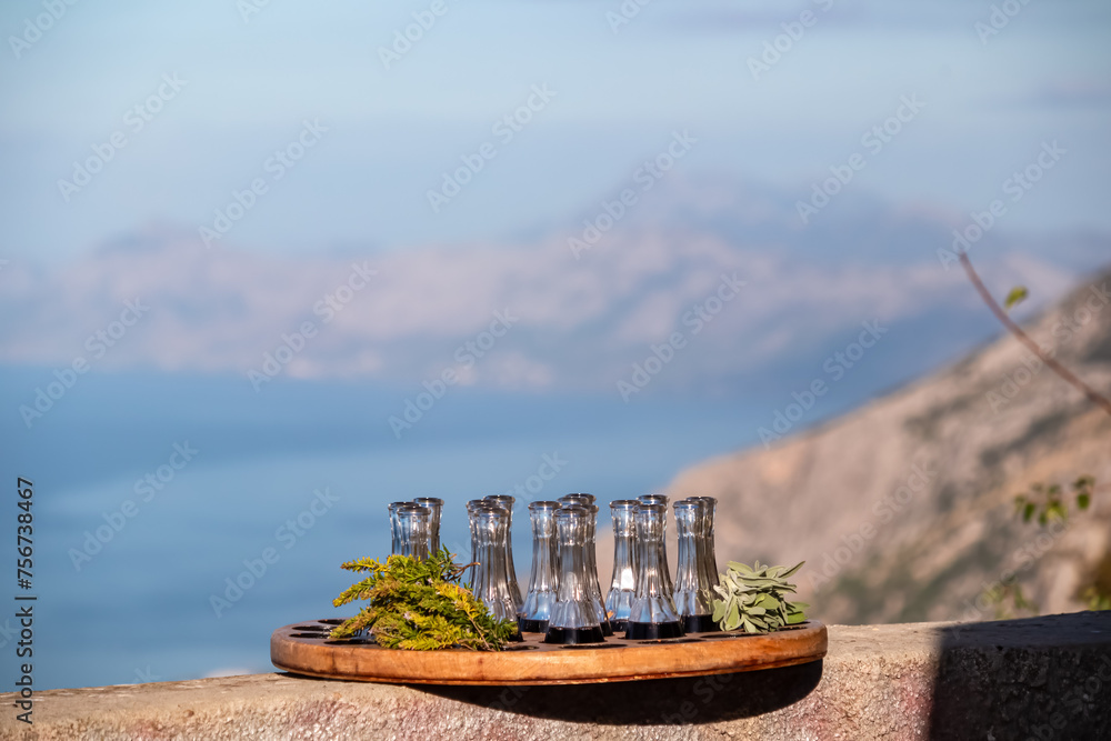 Wooden plate with strong sweet Croatian aperitif fruity drinks like slivovitz, kruskovac and rakija. Panoramic aerial view of Makarska Riviera in Biokovo, Dalmatia, Croatia. Typical traditional liquor