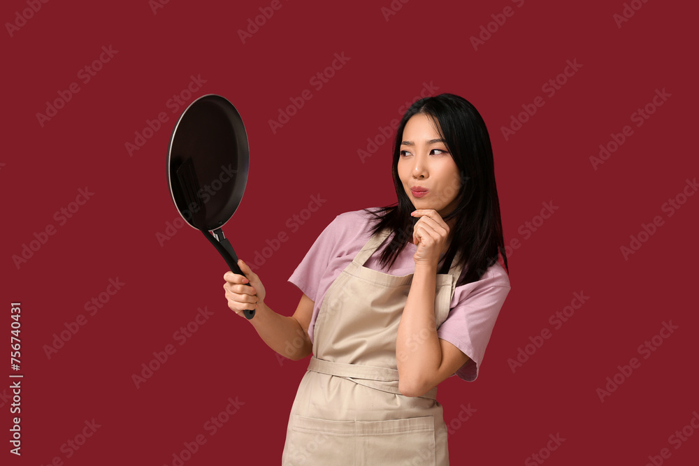 Portrait of thoughtful Asian woman with frying pan on red background Portrait of thoughtful Asian woman with frying pan on red background