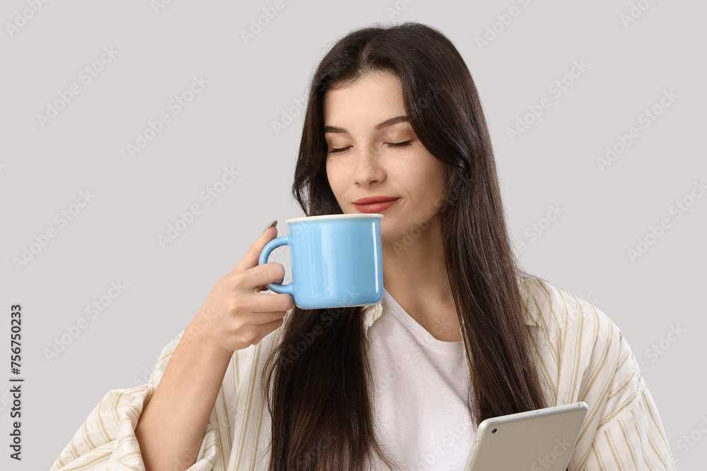 Beautiful young woman with mug of tea and tablet computer on grey background Beautiful young woman with mug of tea and tablet computer on grey background