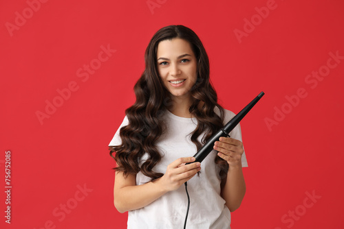 Beautiful young woman with curling iron on red background