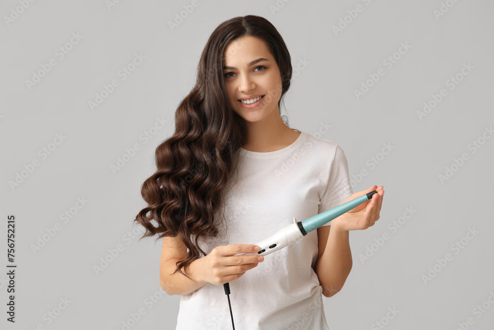 Beautiful young woman with curling iron on grey background Beautiful young woman with curling iron on grey background