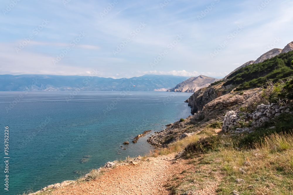 Idyllic hiking trail along rugged cliffs in coastal town Baska, Krk Island, Primorje-Gorski Kotar, Croatia, Europe. Vacation in turquoise water bay. Majestic coastline of Mediterranean Adriatic Sea