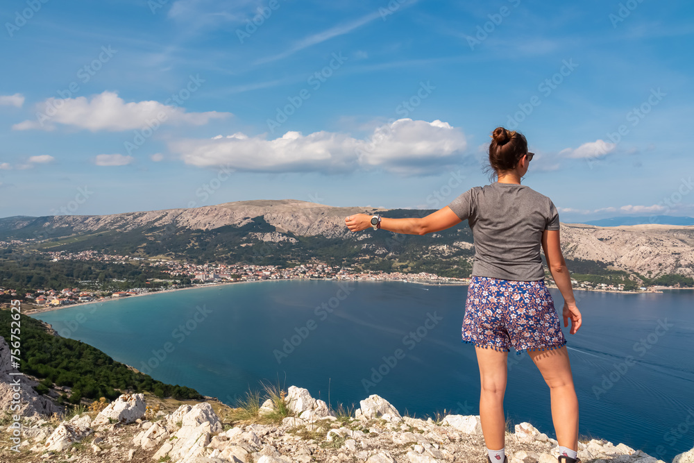 Active woman on scenic hiking trail with panoramic aerial view of idyllic lagoon in coastal town Baska, Krk Island, Primorje-Gorski Kotar, Croatia, Europe. Coastline of Mediterranean Adriatic Sea