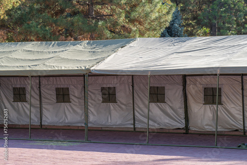 Quickly deployable multi-person khaki tent with windows and reflective lining inside. The tent is set up amidst a pine forest on a campsite. photo