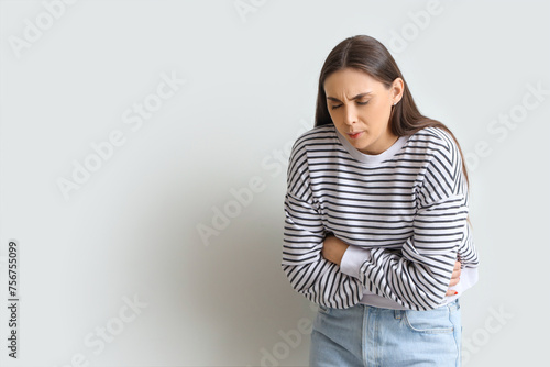 Young woman suffering from bellyache on light background