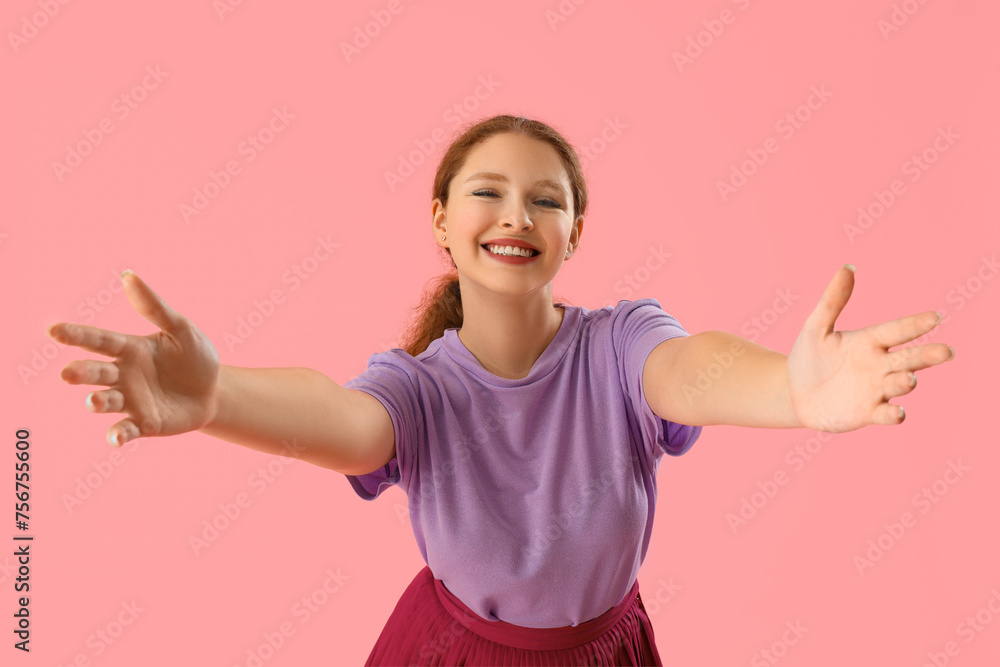 Smiling young redhead woman opening arms for hug on pink background Smiling young redhead woman opening arms for hug on pink background