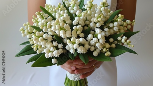 a bouquet of lily of the valley flowers being held by a woman's hand on a white table cloth. photo