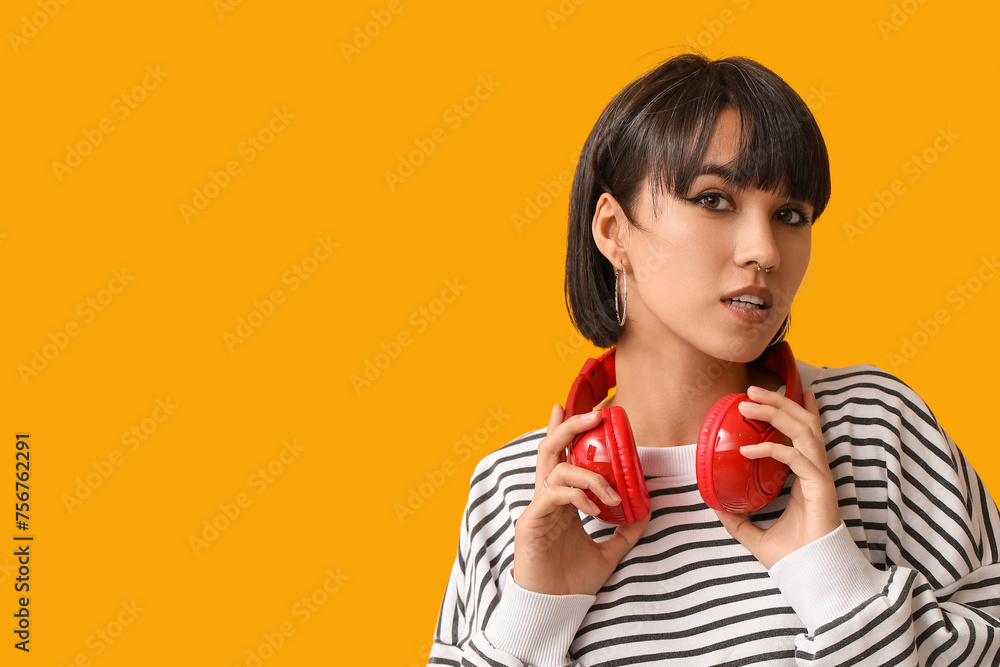 Stylish young woman with nose piercing and headphones on yellow background Stylish young woman with nose piercing and headphones on yellow background