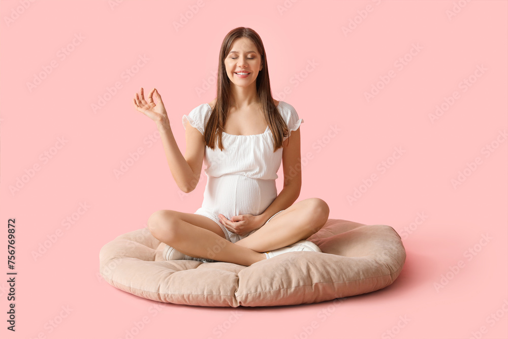 Young pregnant woman meditating on pouf against pink background Young pregnant woman meditating on pouf against pink background