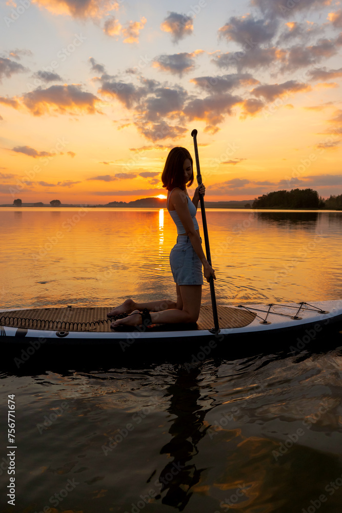 athletic woman on SUP paddle boarding through shining water at sunset. aesthetically wide shot. Freedom happy female relaxing on surfboard on a lake