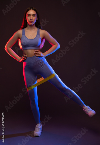 A slender female bodybuilder in a lilac tracksuit is doing an exercise with an expander on her legs, doing cardio. Sports concept, fat burning and healthy lifestyle.