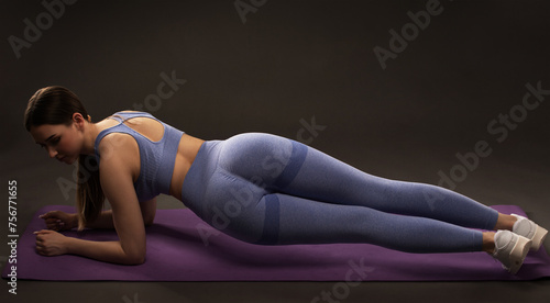 A slender female bodybuilder in a lilac tracksuit does an exercise plank to burn belly fat and does cardio. Sports concept, fat burning and healthy lifestyle.