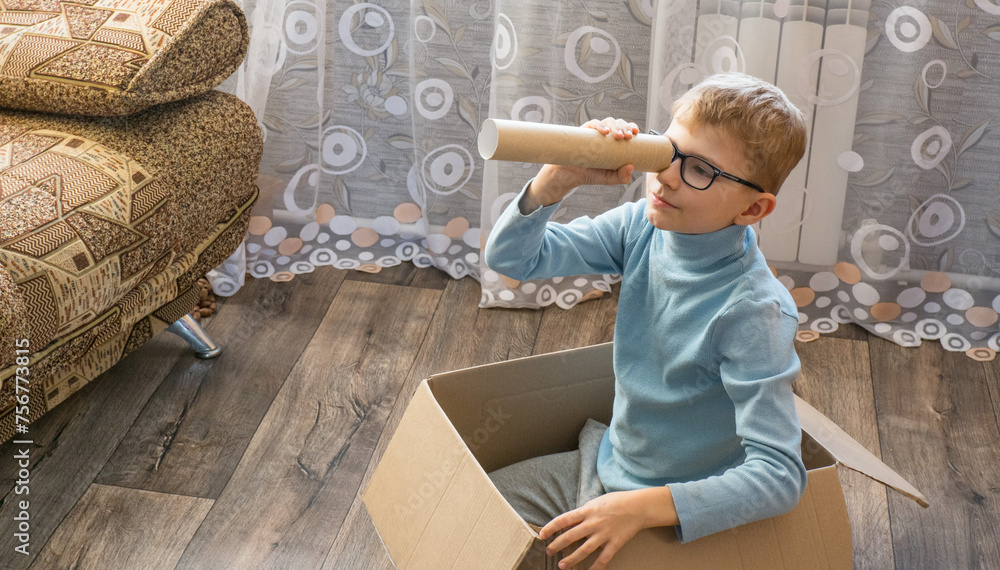 Playful cheerful child, boy looking into a cardboard tube, sitting in a box.