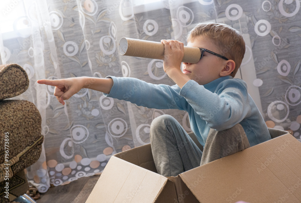 Playful cheerful child, boy looking into a cardboard tube, sitting in a box