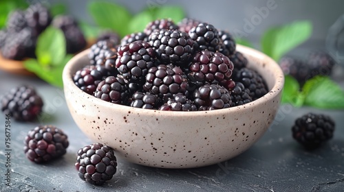 a bowl filled with blackberries on top of a table next to green leaves and a wooden spoon with blackberries in it.