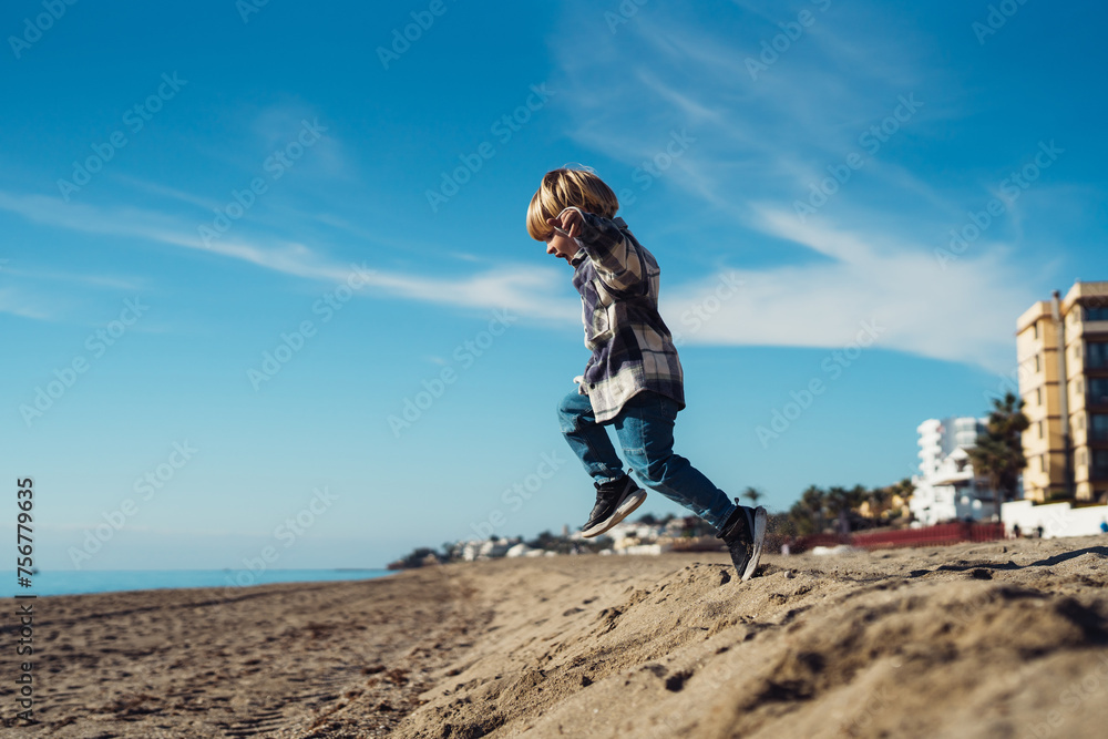 The boy jumps up on the sandy beach near the sea. a 3-year-old boy in a checkered shirt plays on the sand. cheerful active baby jumping on the sand
