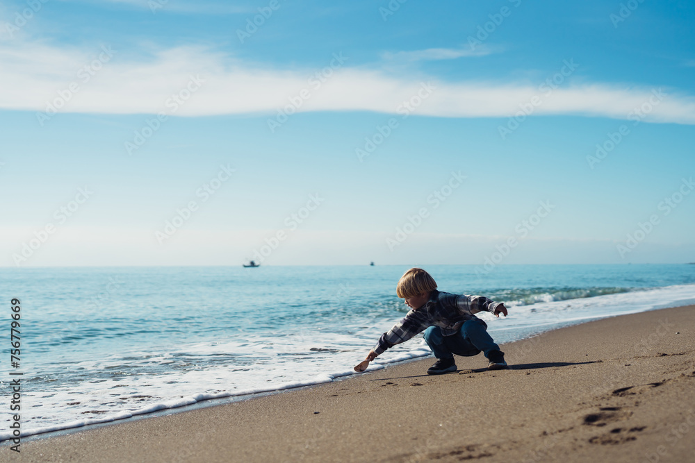 boy 3 years old blond plays on the seashore in the sand with pla - obrazy, fototapety, plakaty 