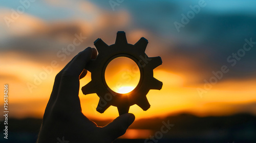 Silhouette of a man holding the round cogwheel or gear part outdoor at the sunset twilight sky in the evening. Symbolizing the system development and optimization, mechanics progress and solution photo