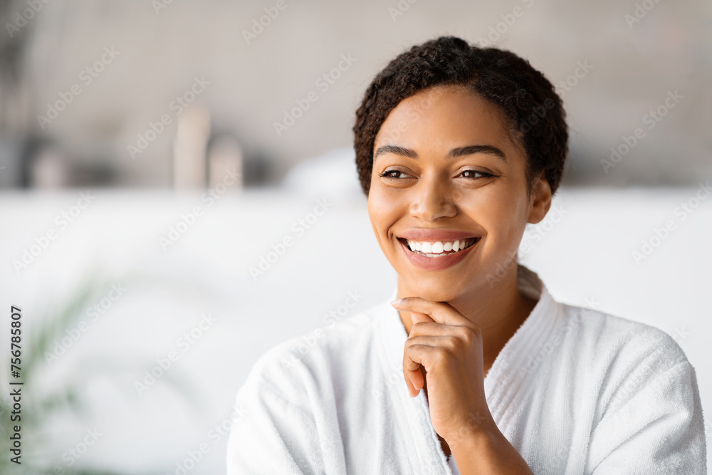 Joyful young black woman in bathrobe touching chin and looking away Joyful young black woman in bathrobe touching chin and looking away