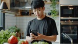 Young asian man in the kitchen looking at her phone checking a recipe for cooking -