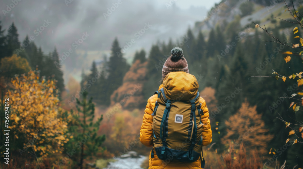A lone hiker in a yellow jacket gazes at the misty mountains during autumn, surrounded by vibrant fall foliage.