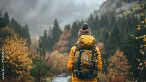 A lone hiker in a yellow jacket gazes at the misty mountains during autumn, surrounded by vibrant fall foliage.