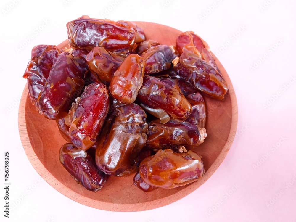 Close up of dates isolated on pink background. a pile of dates served on a wooden plate on a pink background. sweet brown fruit. healthy meals. food for breaking the fast Close up of dates isolated on pink background. a pile of dates served on a wooden plate on a pink background. sweet brown fruit. healthy meals. food for breaking the fast