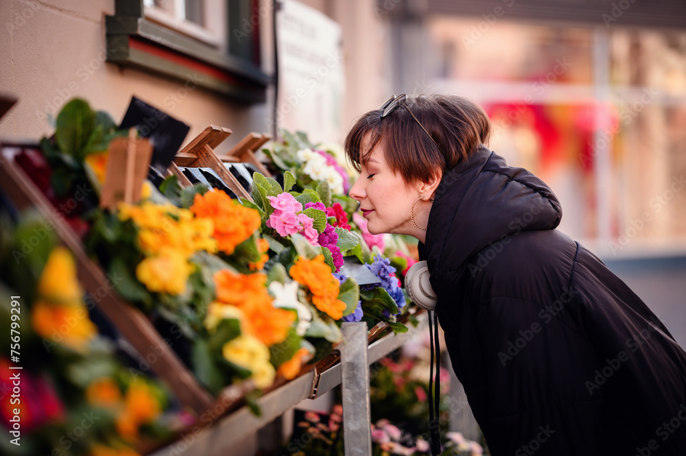 Fototapeta premium A woman leans in to savor the fragrance of bright, fresh flowers at an outdoor market, creating a sensory connection amidst the urban hustle