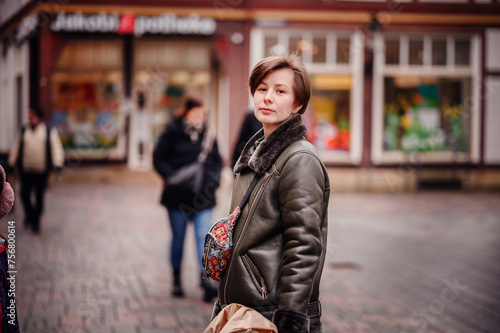 A stylish woman in a chic leather jacket holds a bouquet and a shopping bag, her poised look reflecting a successful day of shopping in the city.