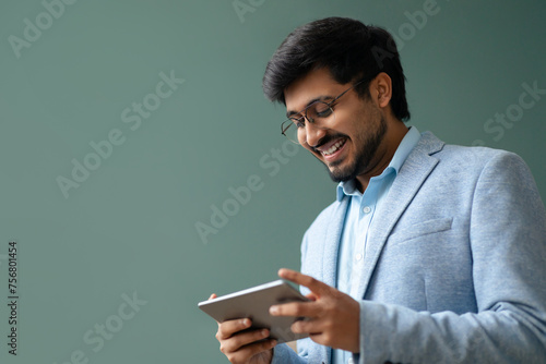 Foto Happy hindu businessman websurfing on digital tablet against green wall