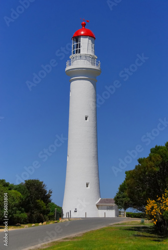 A white and red lighthouse stands tall against a clear blue sky on a beautiful sunny day.