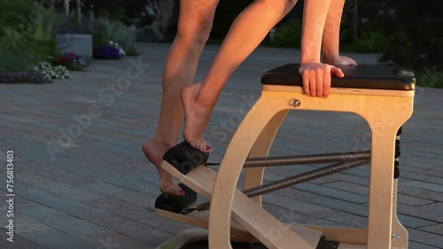 Working on footwork on a reformer pilates chair. Close-up of a female athlete's feet. Effective pilates training in modern studio blonde woman stretching back and leg muscles on reformer 