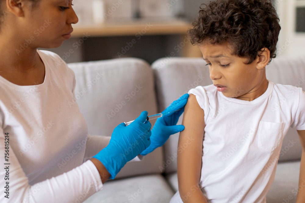 Black doctor woman in gloves making vaccination for little boy at home Black doctor woman in gloves making vaccination for little boy at home