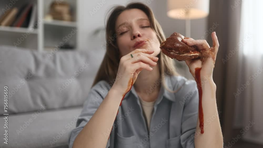 Portrait of funny happy young woman eating burger with great pleasure while ketchup flows down the hands at home Excited hungry female biting hamburger enjoying fast junk food indoors Portrait of funny happy young woman eating burger with great pleasure while ketchup flows down the hands at home Excited hungry female biting hamburger enjoying fast junk food indoors