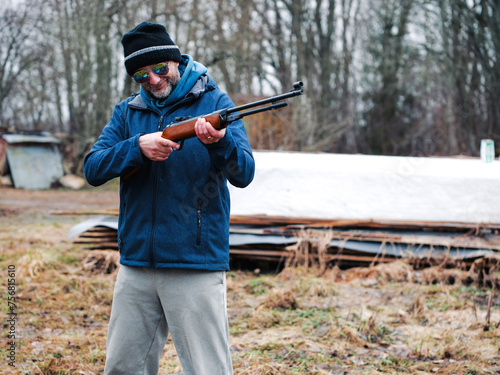 Man with old style rifle with wooden base and stock and simple iron sight in a country rural area. Airsoft or BB gun outdoor practice. Male model with grey beard. Hunting practice.