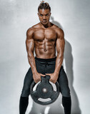 Athletic man doing exercise with heavy weights plate. Photo of man with naked torso on grey background. Strength and motivation