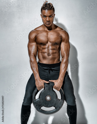 Athletic man doing exercise with heavy weights plate. Photo of man with naked torso on grey background. Strength and motivation