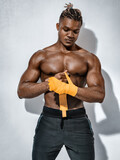 Boxer man with naked torso, wrapping his hands in yellow box bandages on gray background. Strength and motivation