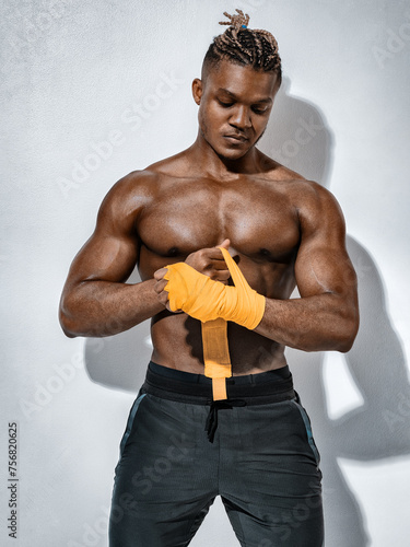 Boxer man with naked torso, wrapping his hands in yellow box bandages on gray background.  Strength and motivation