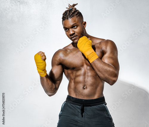 Boxer training. Photo of athletic african american man with naked torso, his arms wrapped in yellow bandages on gray background.  Strength and motivation